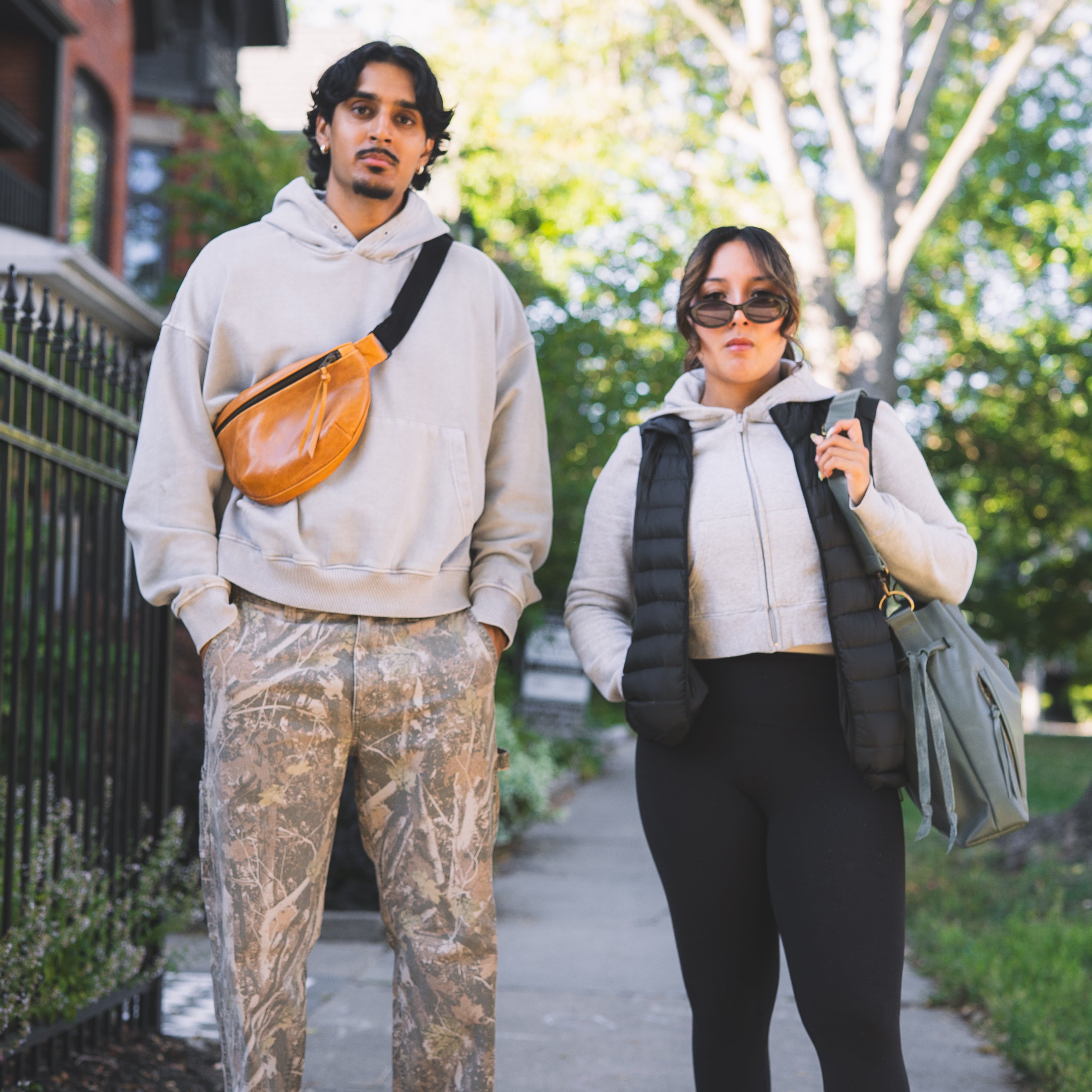 Two people walking on a sidewalk with trees and buildings in the background