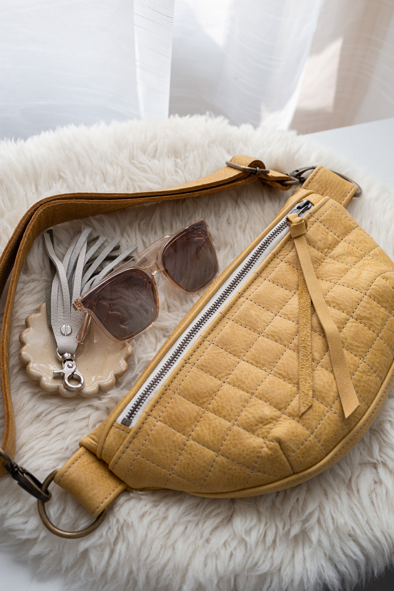 Yellow quilted handbag with sunglasses and a keychain on a white fur surface