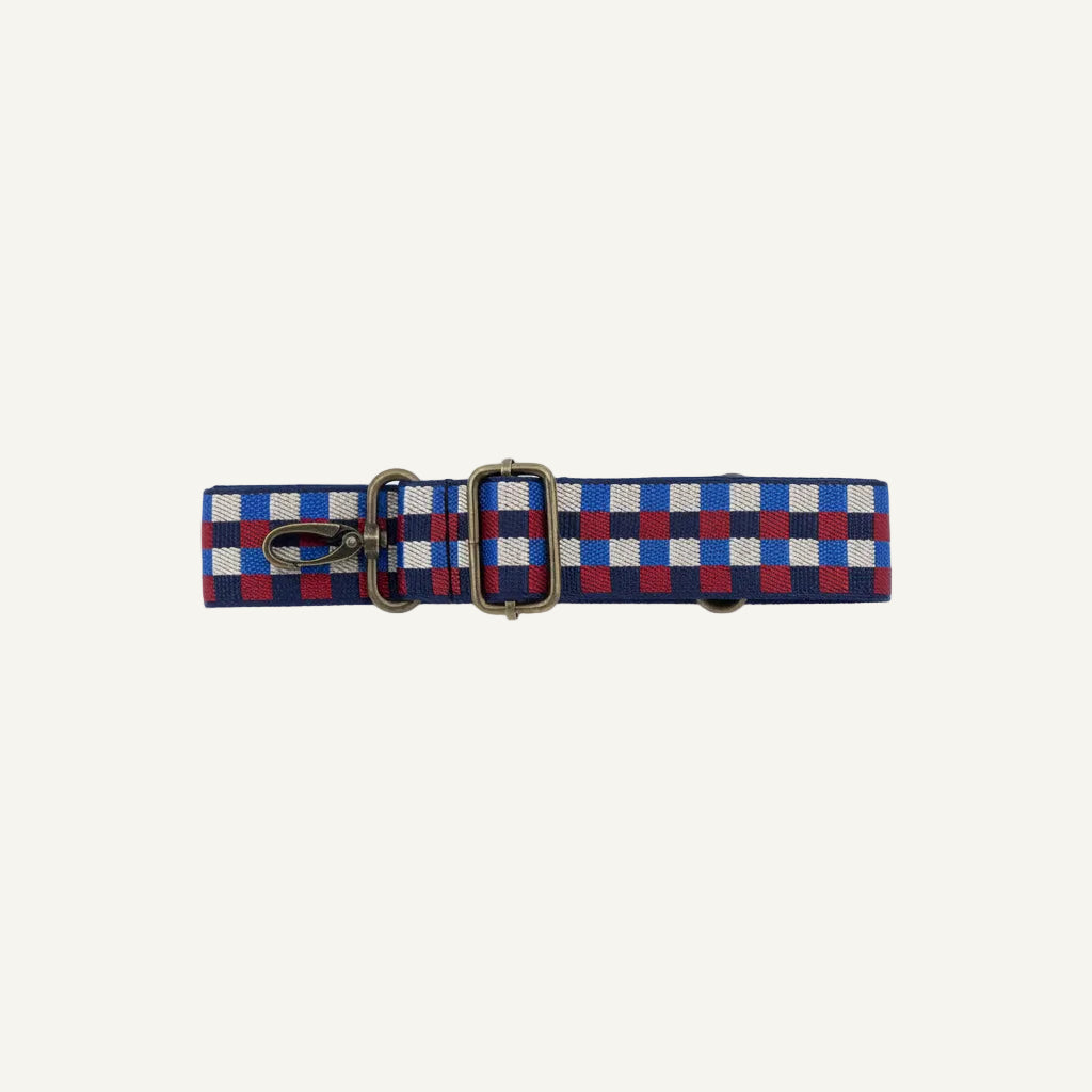 A woven checkered strap with a brass buckle and clasp, featuring a pattern of blue, red, and white squares, laid flat on a white background.