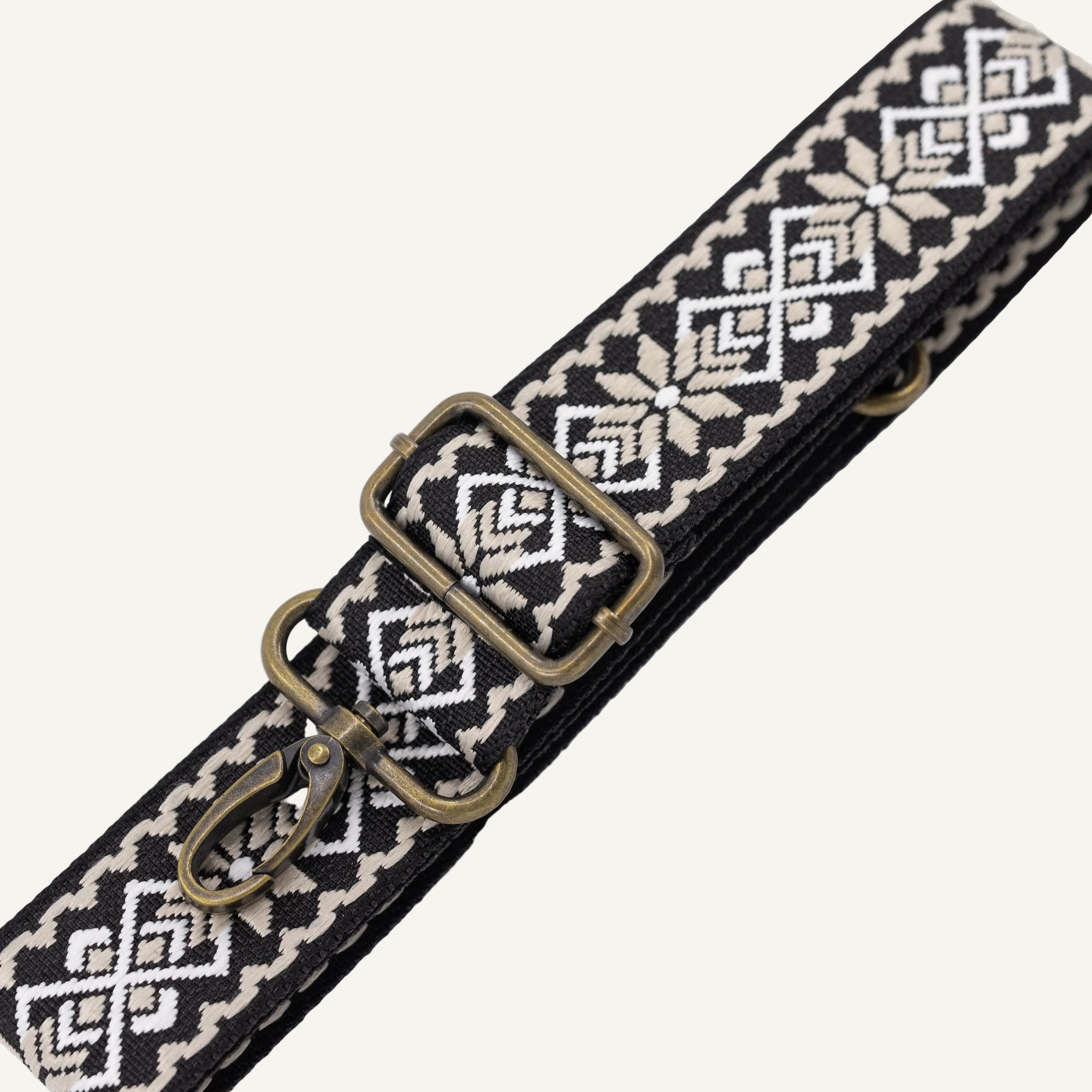 Black and white patterned belt with brass clip on a white background