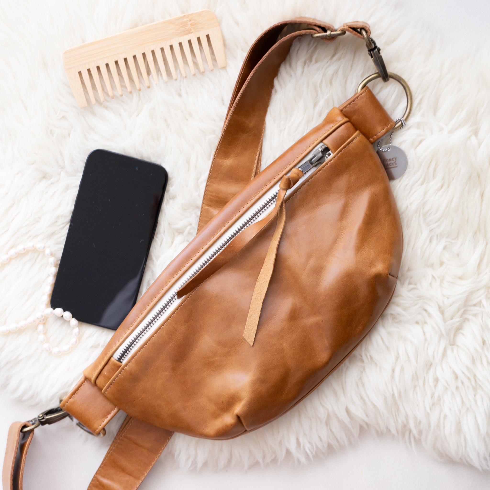 Brown leather bag with phone, comb, and tags on a white surface