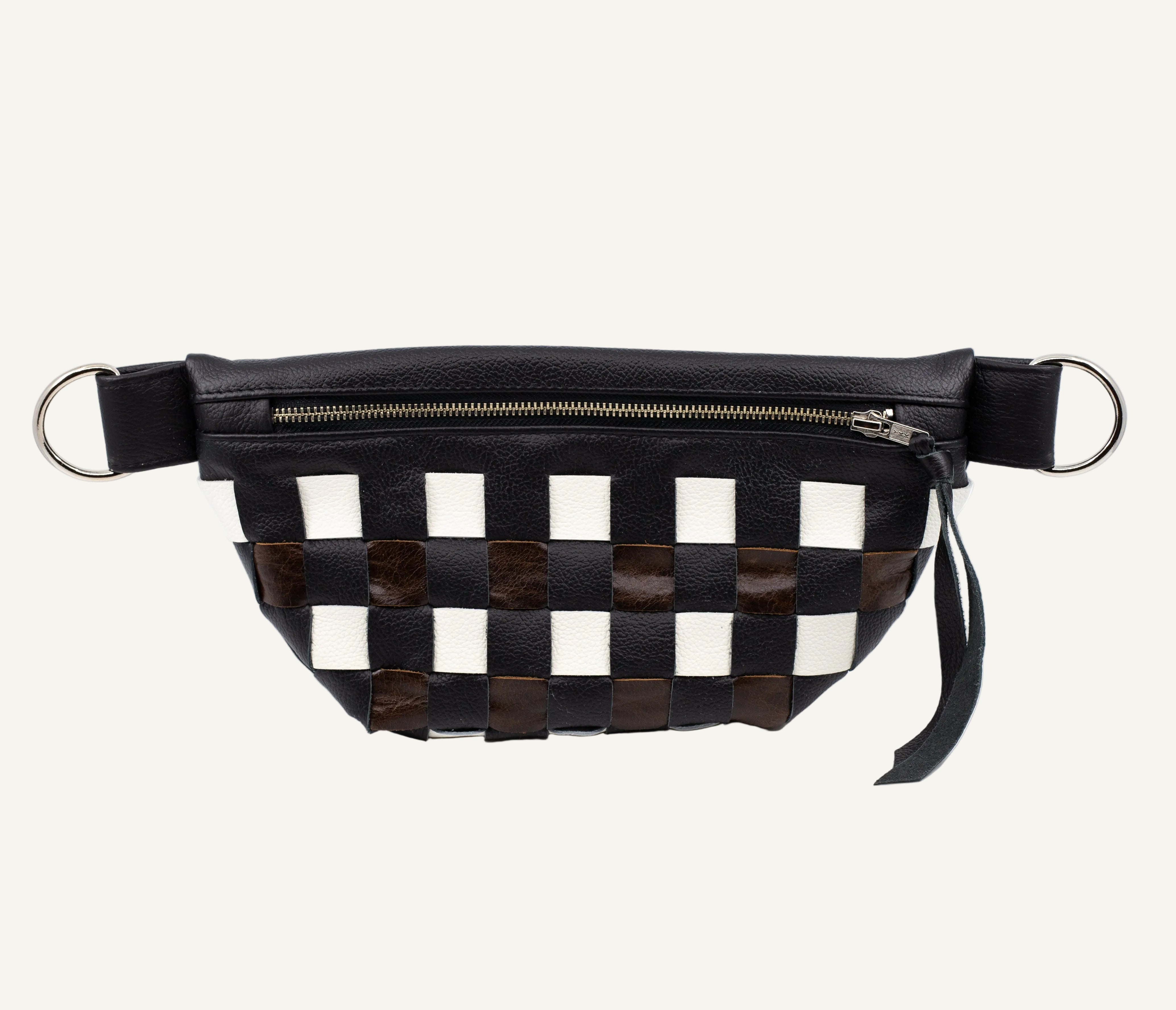 A black leather belt bag featuring a woven checkerboard pattern with black, white, and dark brown patches. It has a top zipper, silver-tone metal D-rings on the sides.