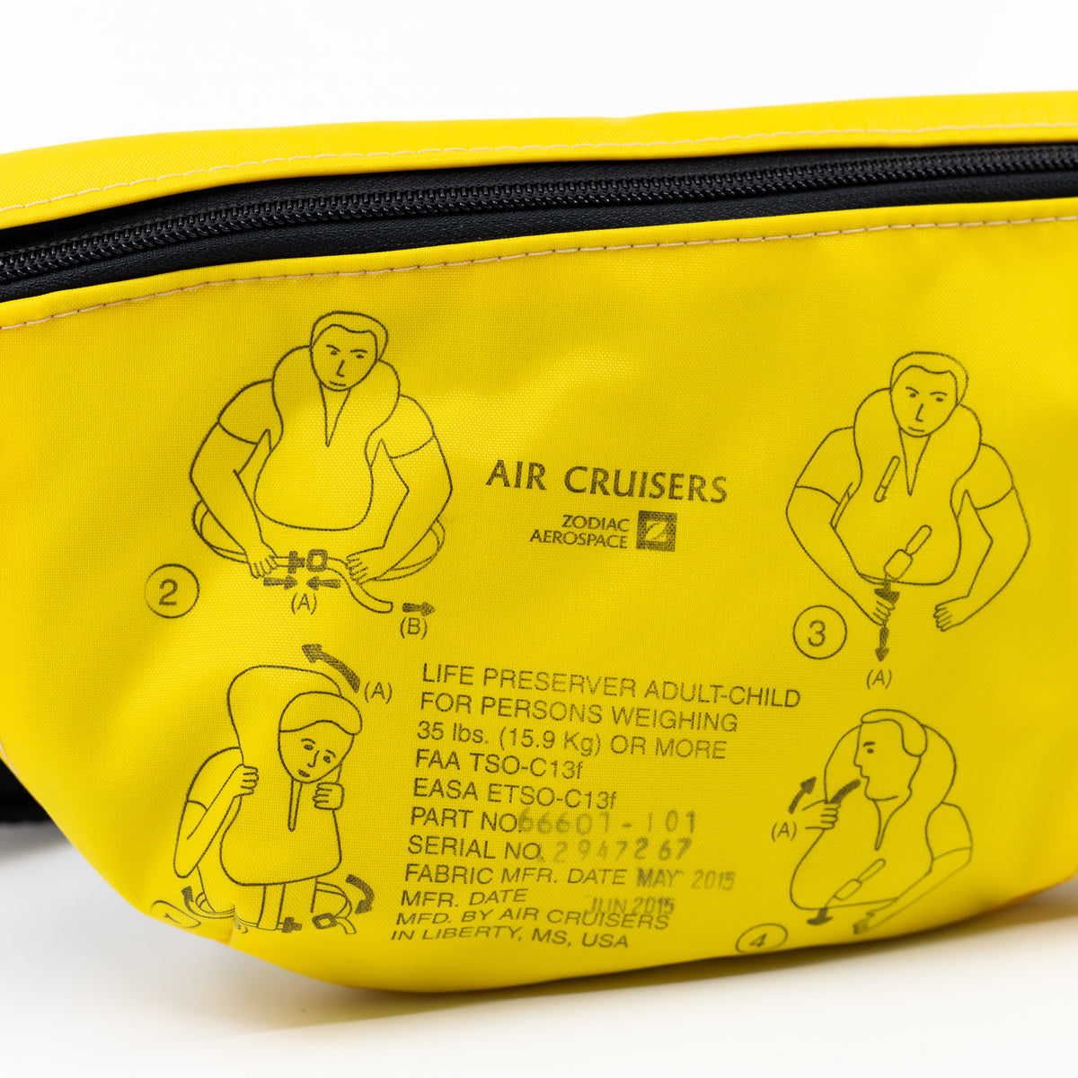 A close-up of a bright yellow life preserver instruction pouch featuring black printed diagrams and text explaining how to wear an air crocodile life preserver, with a black zipper along the top.