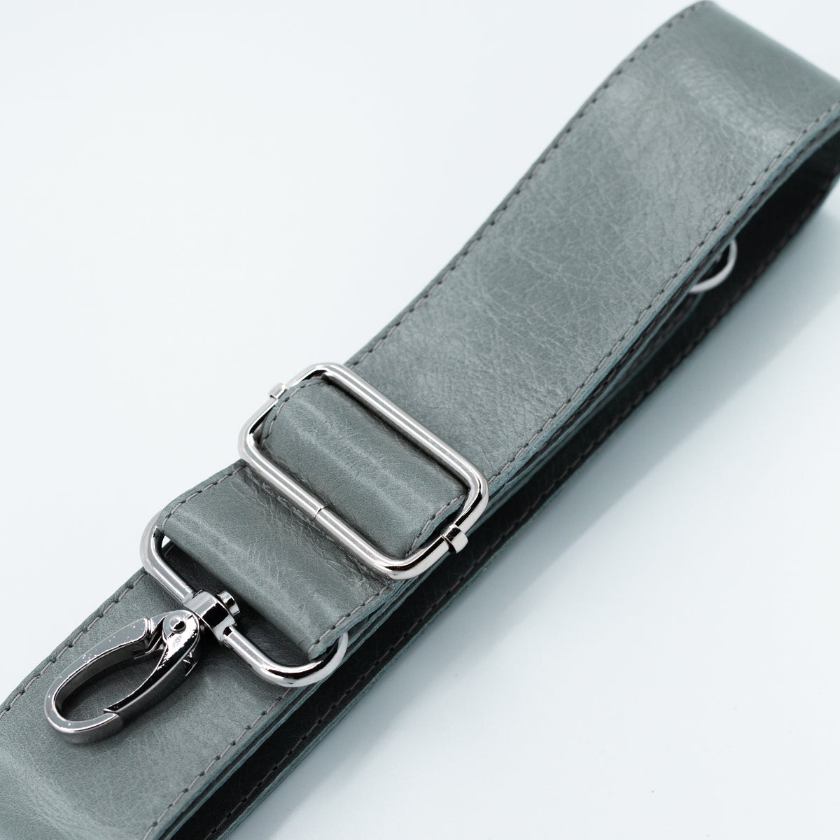 A close-up of a gray leather strap with silver metal hardware, including a rectangular buckle and a lobster clasp, on a clean white background.