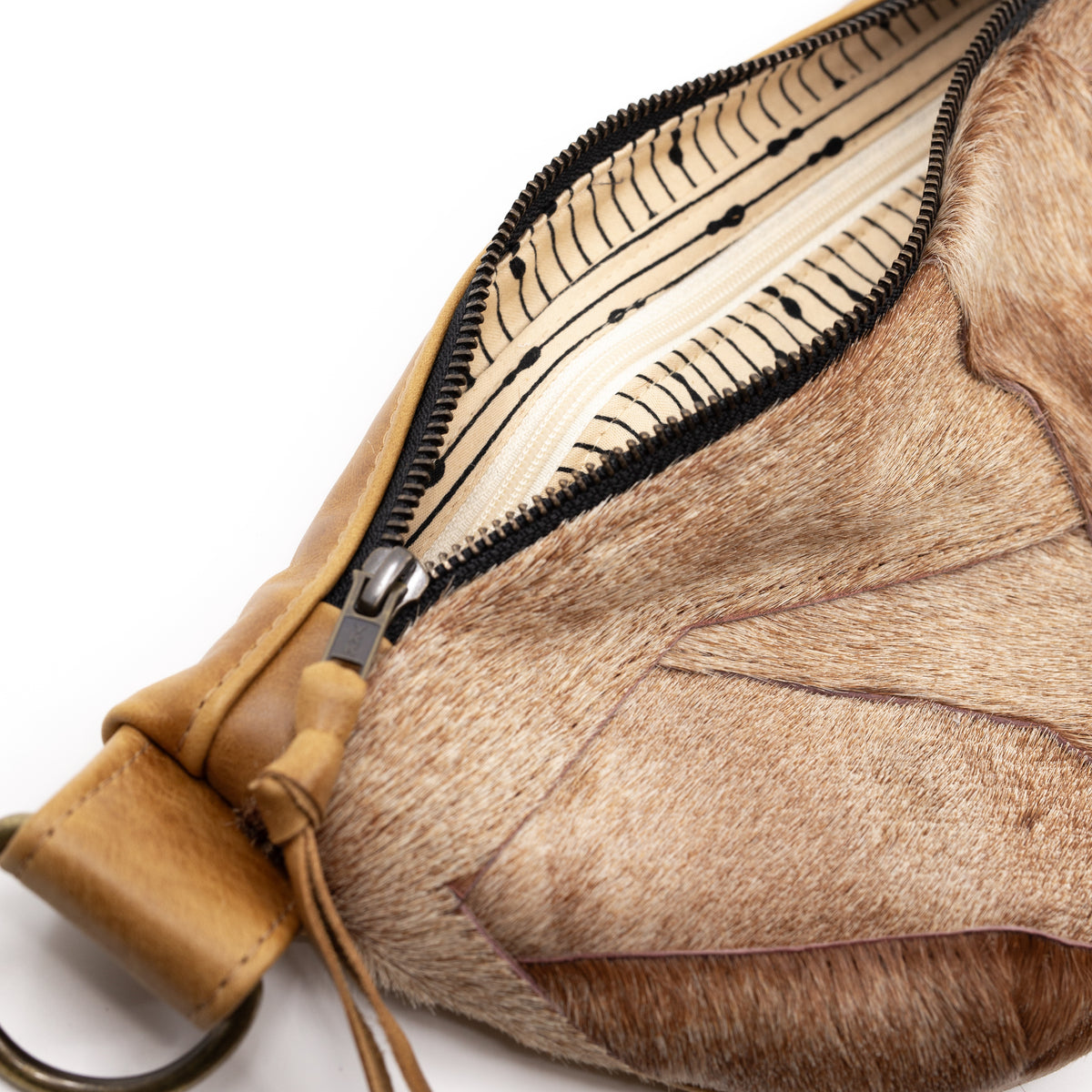 Close-up of a shoulder bag with tan leather trim and a brown animal-hair or fur-like body, shown open to reveal a cream patterned interior lining and black zipper.