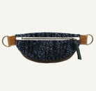 A dark blue and black speckled fabric waist bag, brass hardware, and a green zipper pull, shown against a plain white background.