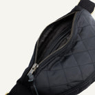 Close-up of a black quilted bag with an open zipper showing the interior lining, on a white background.