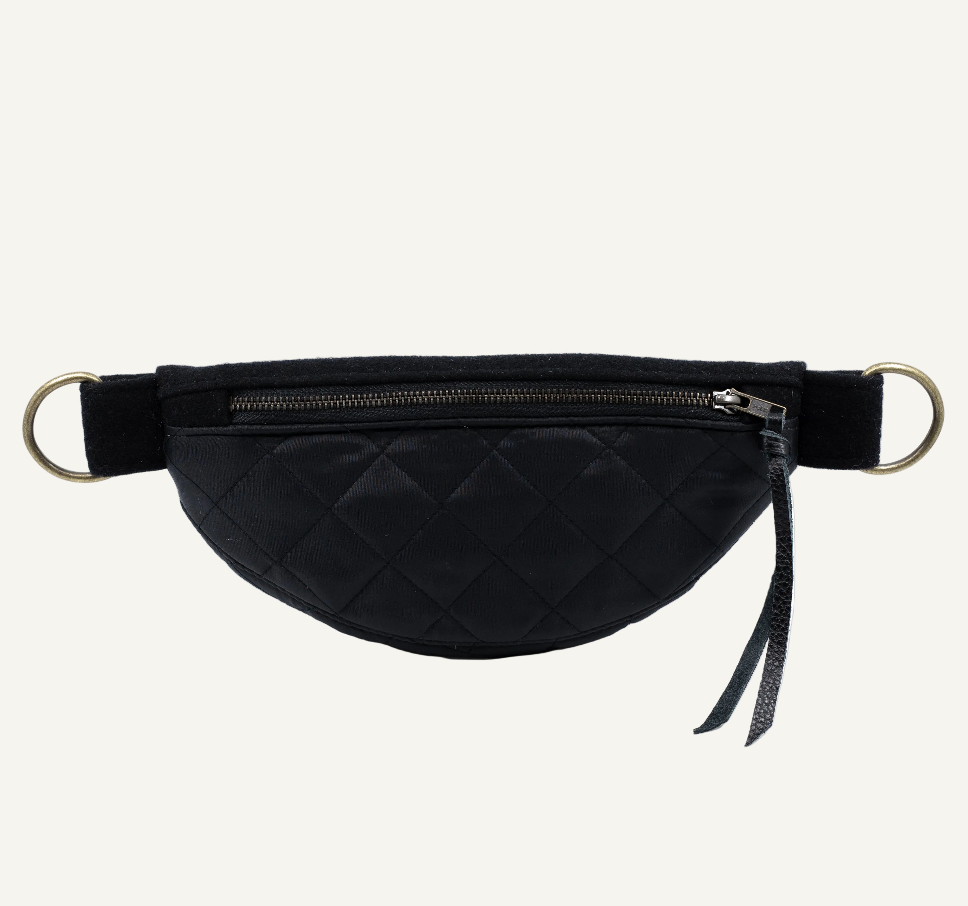 A black quilted waist bag with a diamond-stitched pattern, featuring a top zipper, a black adjustable strap, and gold-tone metal O-rings on a white background.
