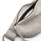 Close-up of a textured light gray fabric bag with an open zipper showing a patterned interior lining, on a white background.
