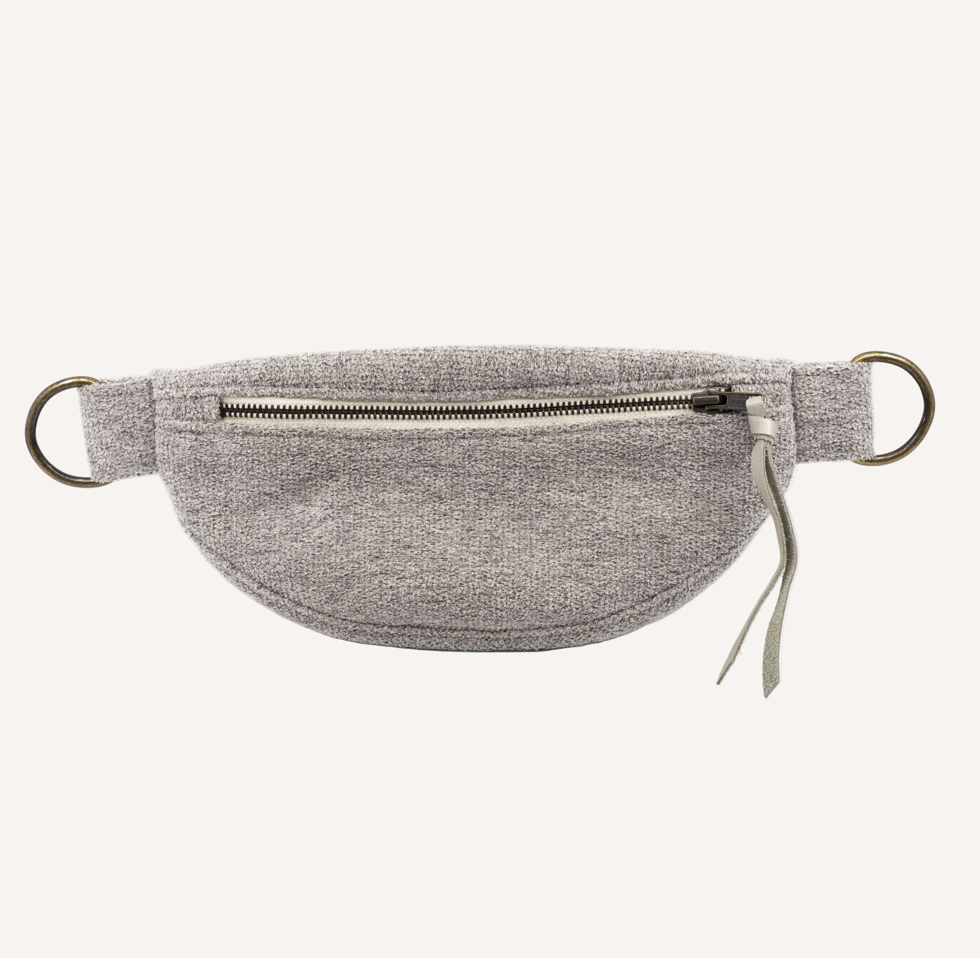 A light gray textured fabric waist bag with a front zipper pocket, bronze metal D-rings, and a small leather pull tab, shown against a plain white background.