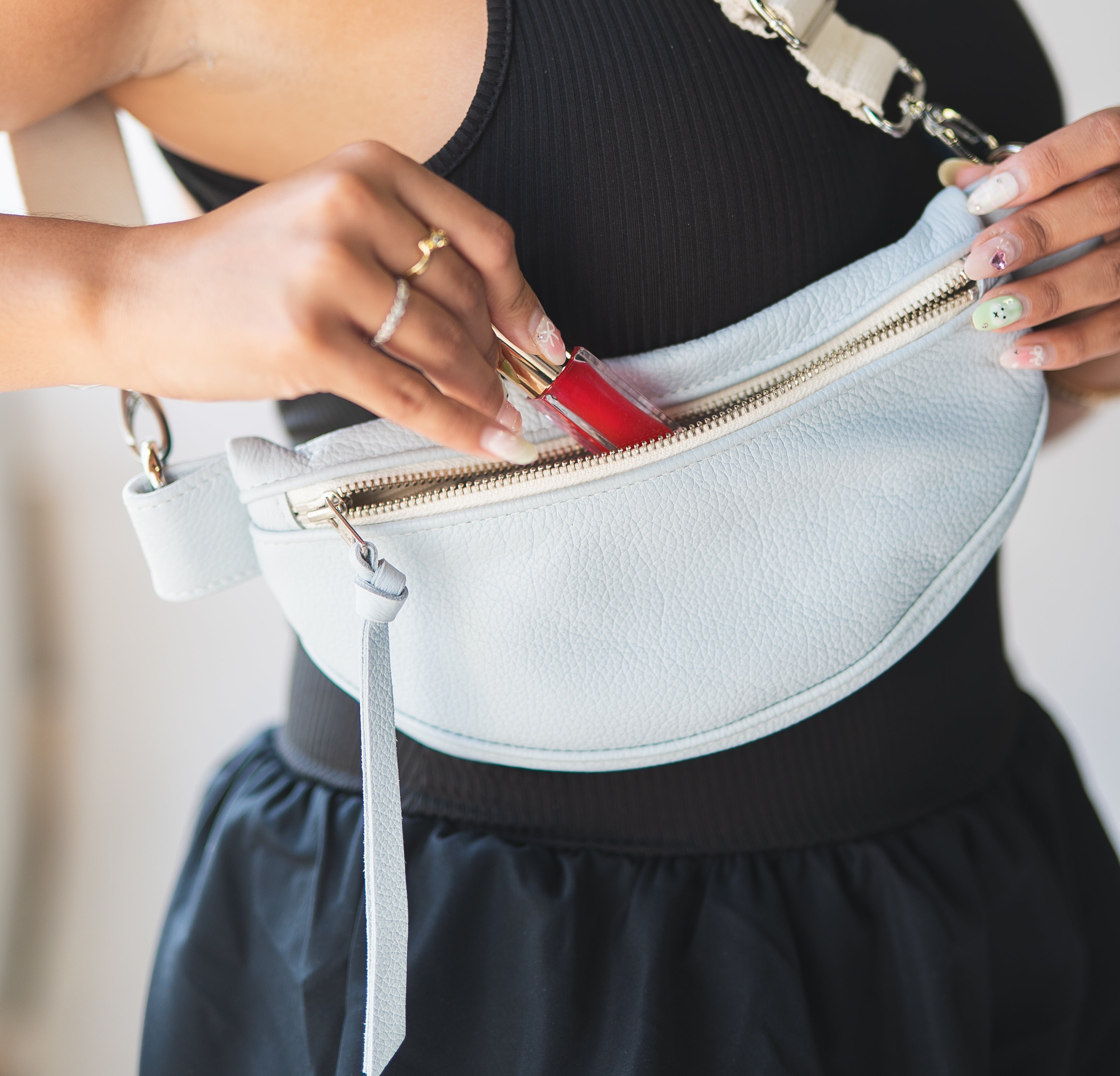 Person holding a white fanny pack with a red item inside, wearing a black top and skirt.