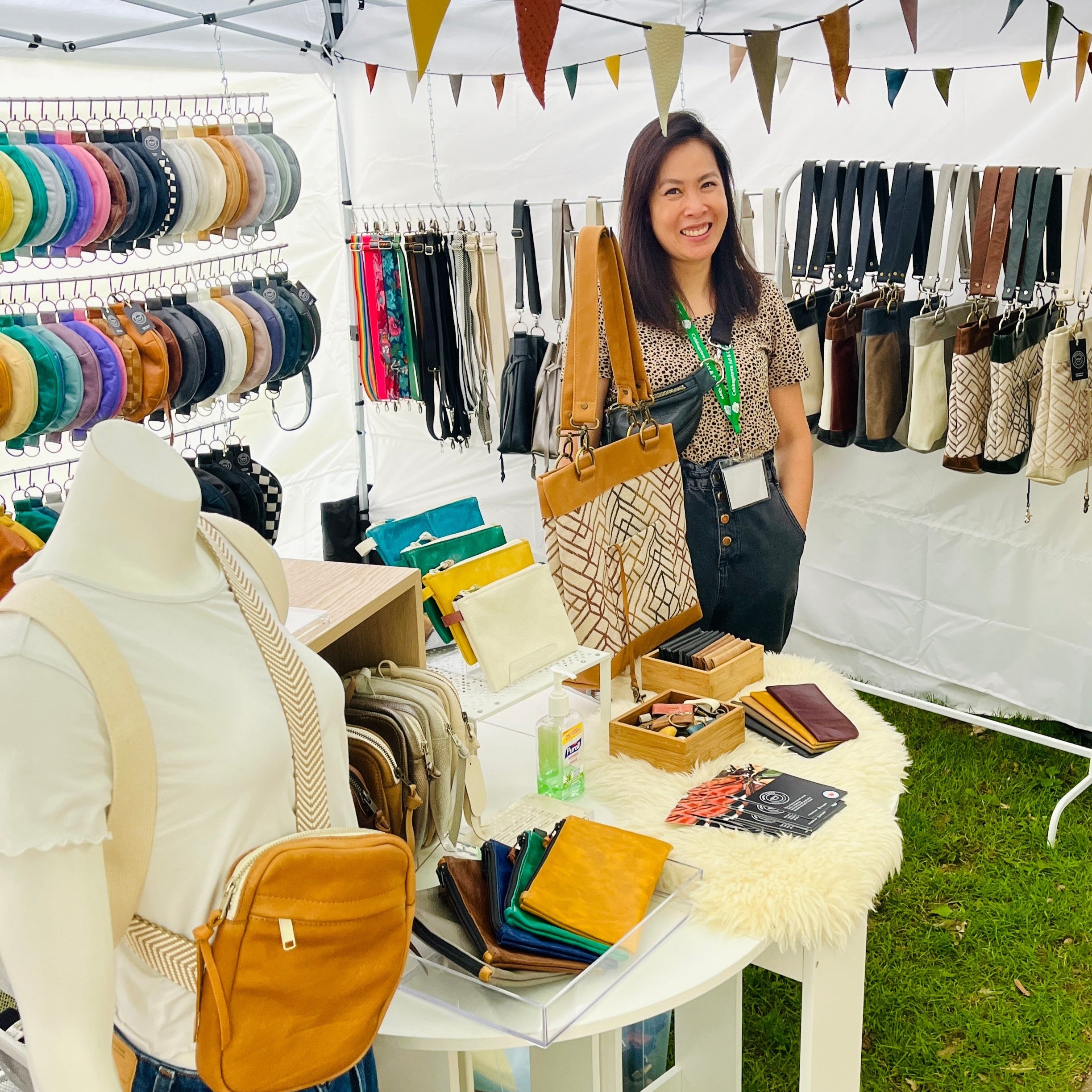 Woman standing behind a table with bags at an outdoor market stall.
