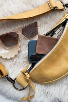 Yellow leather bag with sunglasses, phone case, and wallet on a white fur surface
