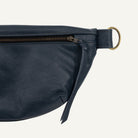 Close-up of a dark navy blue leather belt bag with a brass-tone metal D-ring and zipper pull on a white background.