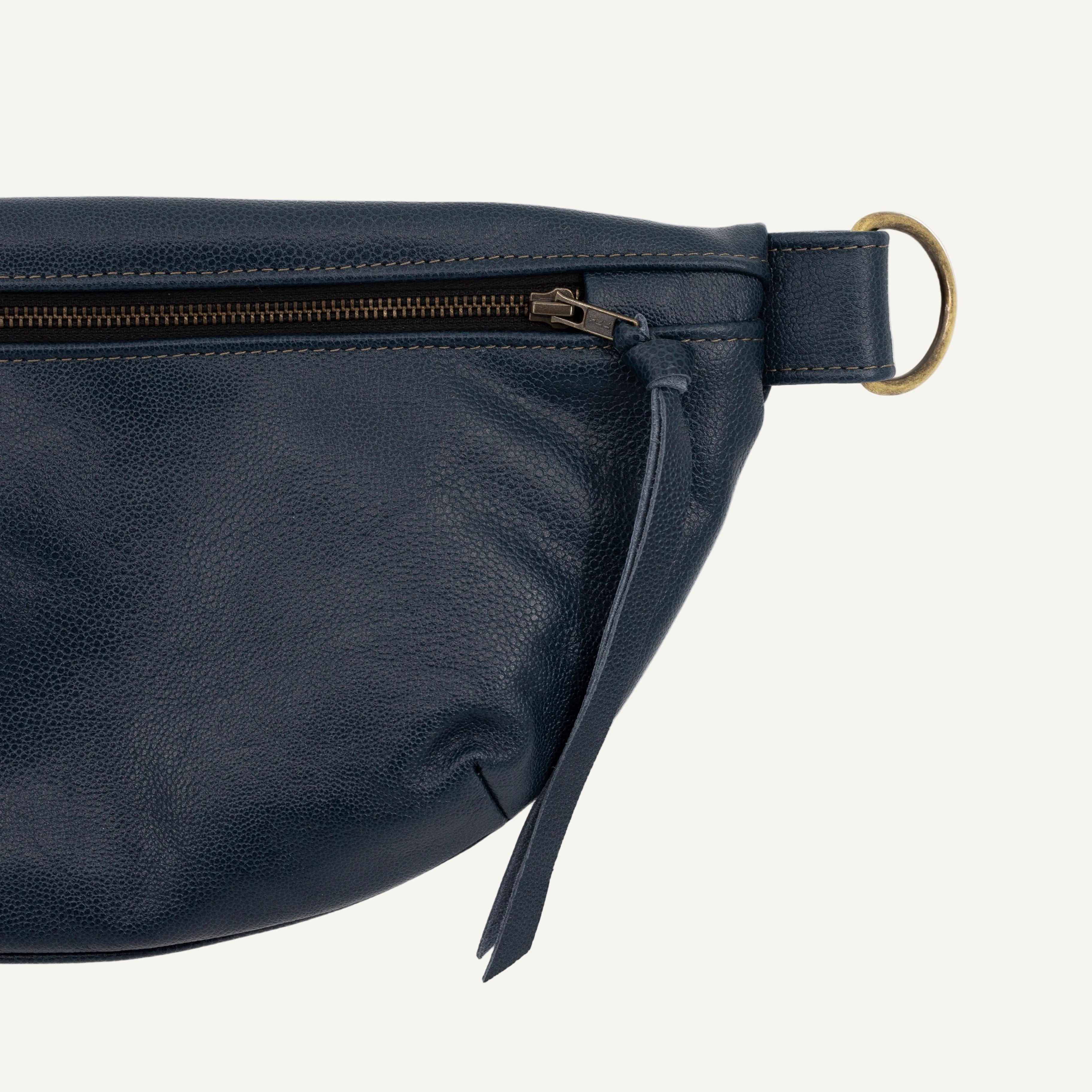 Close-up of a dark navy blue leather belt bag with a brass-tone metal D-ring and zipper pull on a white background.