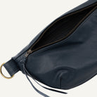 Close-up of a navy blue pebbled leather bag with an open zipper, showing the interior lining and a brass-tone ring detail on a white background.