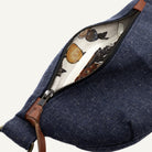 Close-up of a navy blue canvas bag with a partially open zipper, showing a cream-colored interior printed with a vintage-style botanical and bird pattern, and brown leather trim.