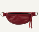 A red leather belt bag with a front zipper, featuring a matching red leather strap with metal rings on each end and a red leather tassel pull, shown against a plain white background.