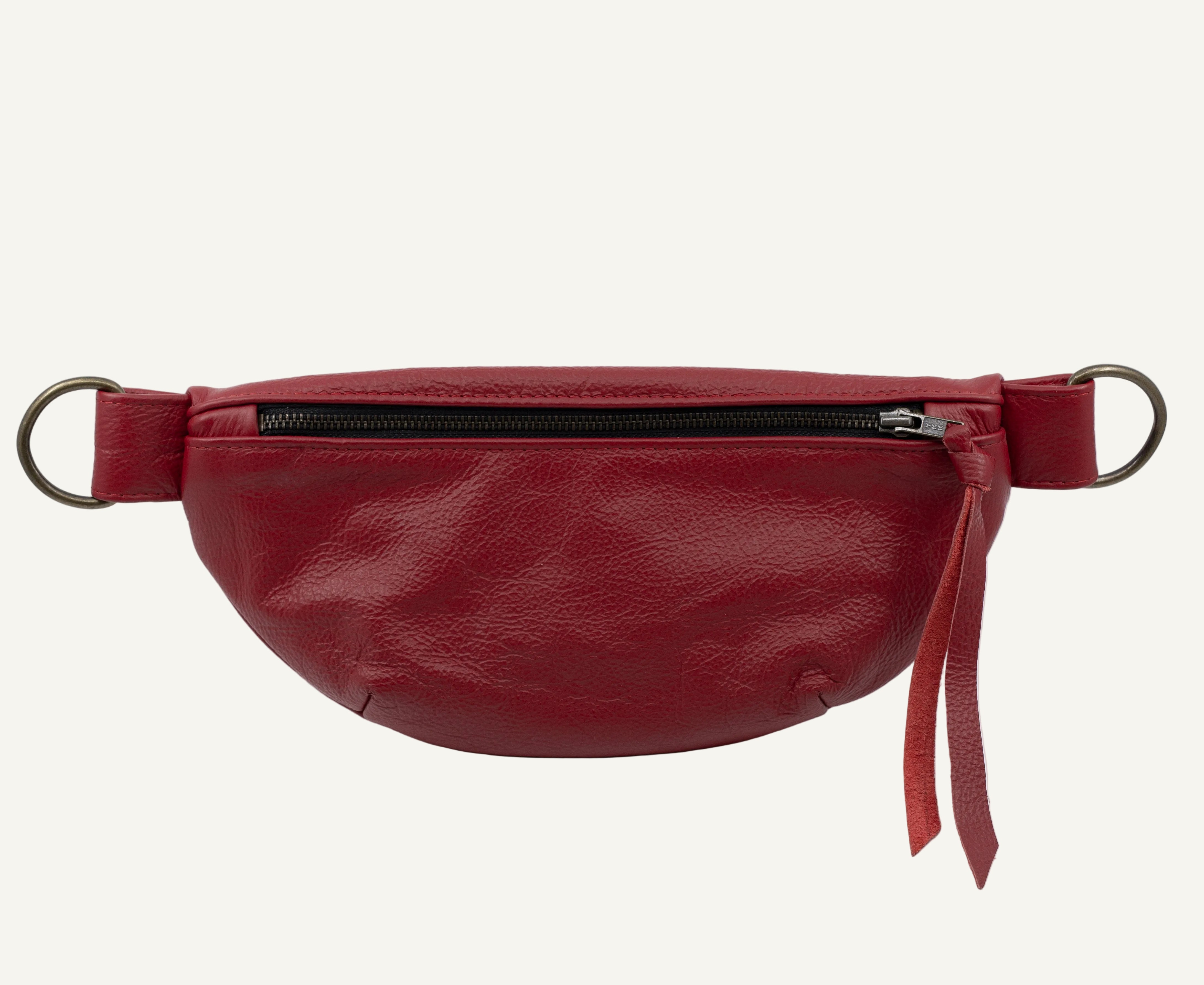 A red leather belt bag with a front zipper, featuring a matching red leather strap with metal rings on each end and a red leather tassel pull, shown against a plain white background.