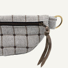 A close-up of a gray and white windowpane plaid fabric pouch with a dark brown leather strap and a gold-tone metal ring.