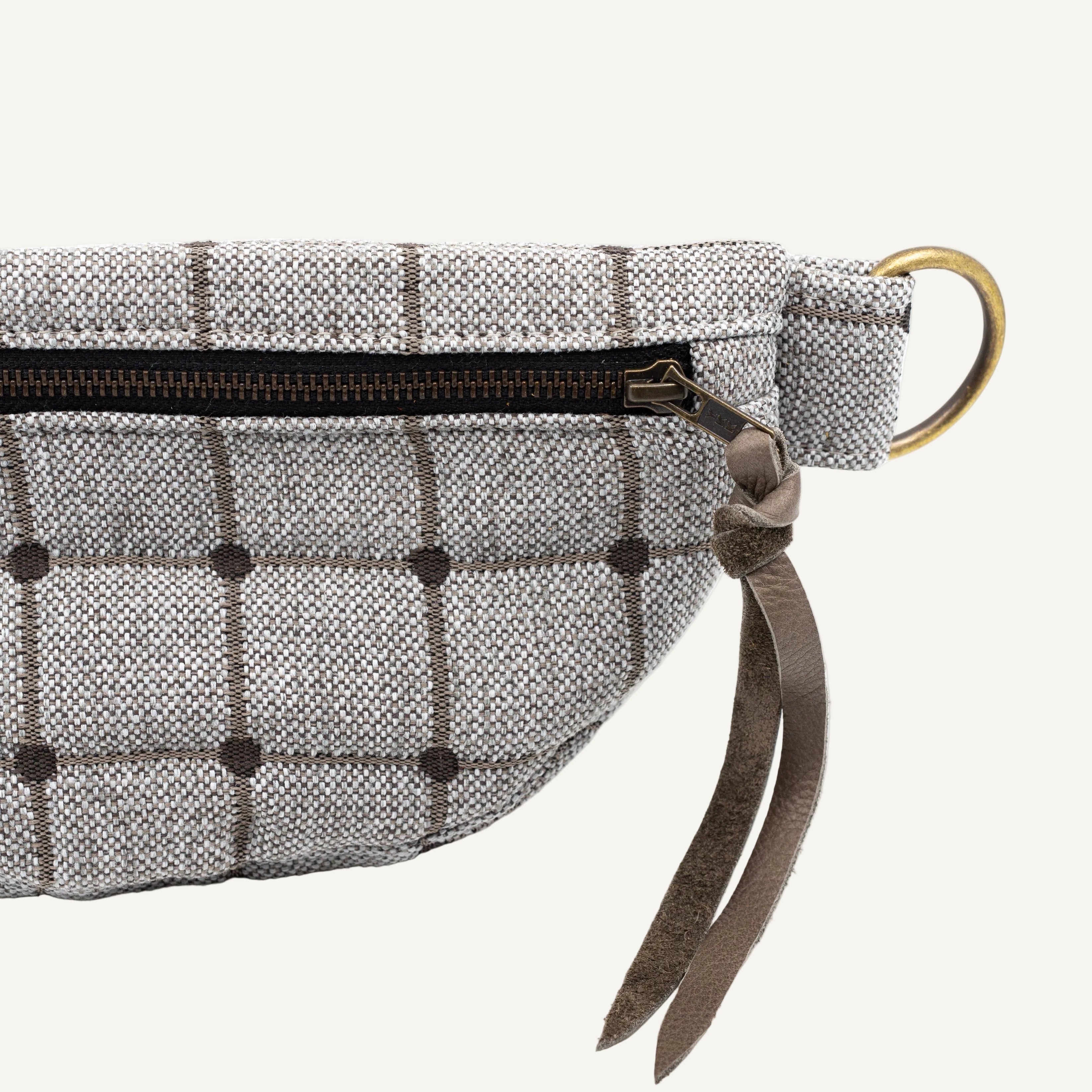 A close-up of a gray and white windowpane plaid fabric pouch with a dark brown leather strap and a gold-tone metal ring.