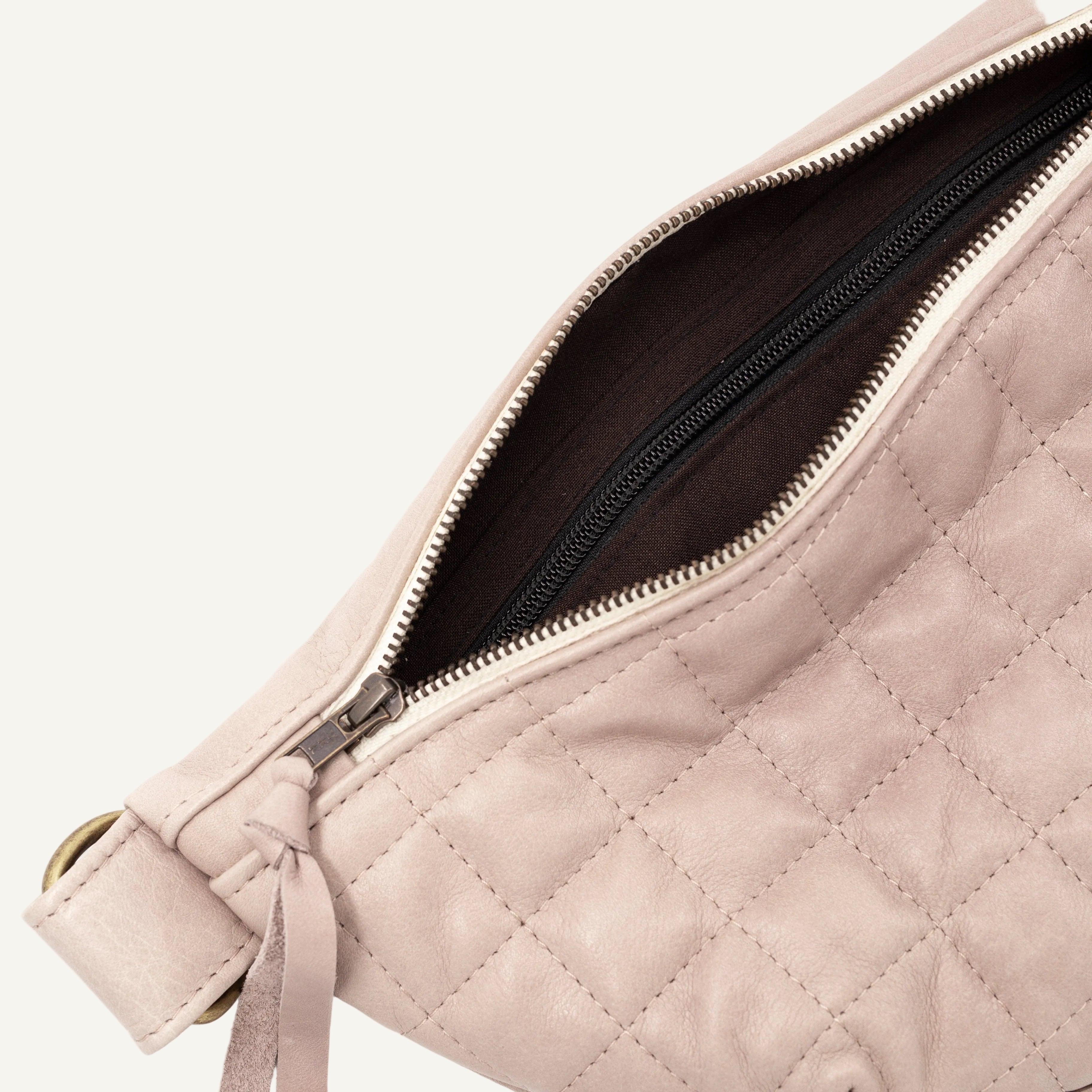 Close-up of a quilted light mauve shoulder bag with a open zipper showing a dark brown interior lining.