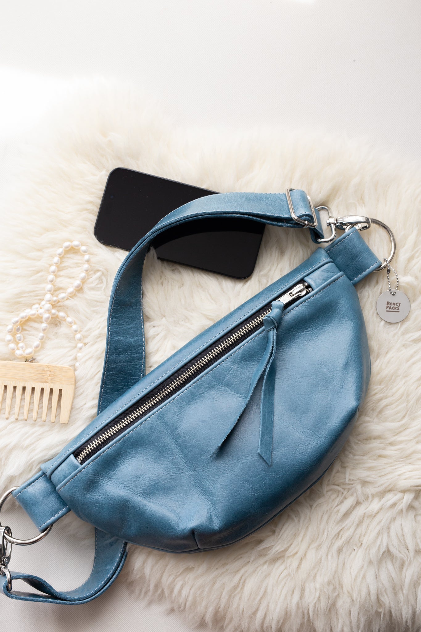 Blue leather bag with a phone and comb on a white fur surface