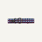 A woven checkered strap with a brass buckle and clasp, featuring a pattern of blue, red, and white squares, laid flat on a white background.