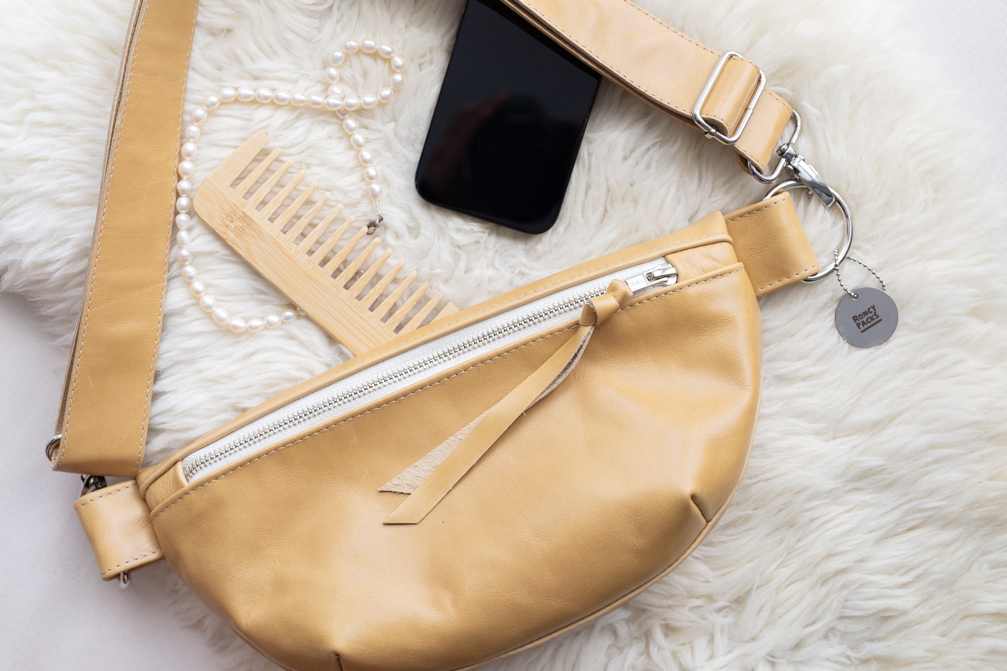 Beige waist bag with a phone and necklace on a white fur surface