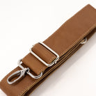 A close-up of a brown leather strap with silver metal hardware, including a rectangular buckle, adjustment loops, and a clip, on a white background.