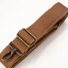 A close-up of a brown leather strap with a brass buckle and a metal clip, shown on a clean white background.