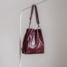 Burgundy leather tote hanging on a rack against a plain background