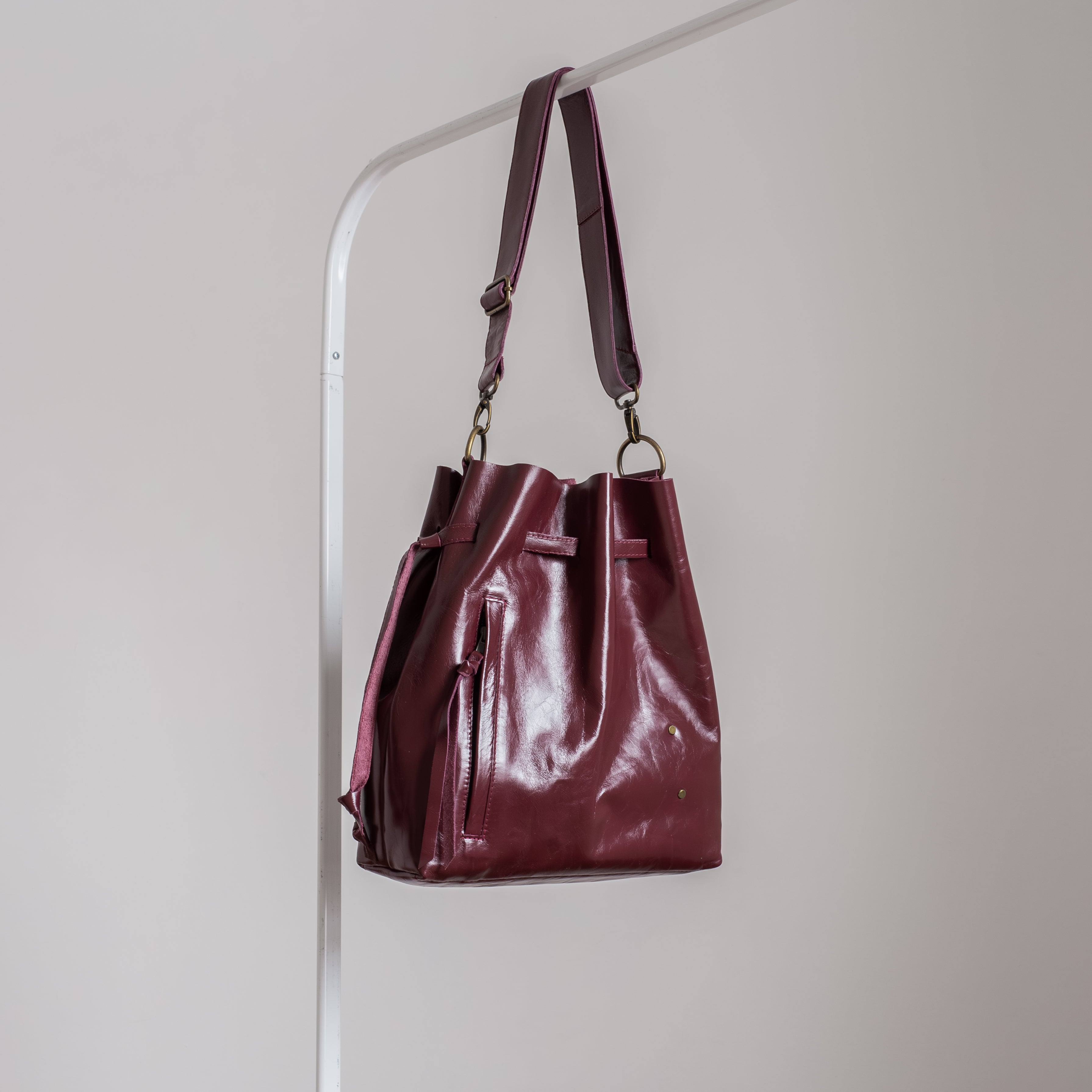 Burgundy leather tote hanging on a rack against a plain background
