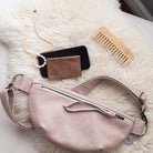 Pink fanny pack, phone, wallet, and comb on a fluffy white surface