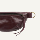 Purple leather waist bag with a gold zipper pull on a white background