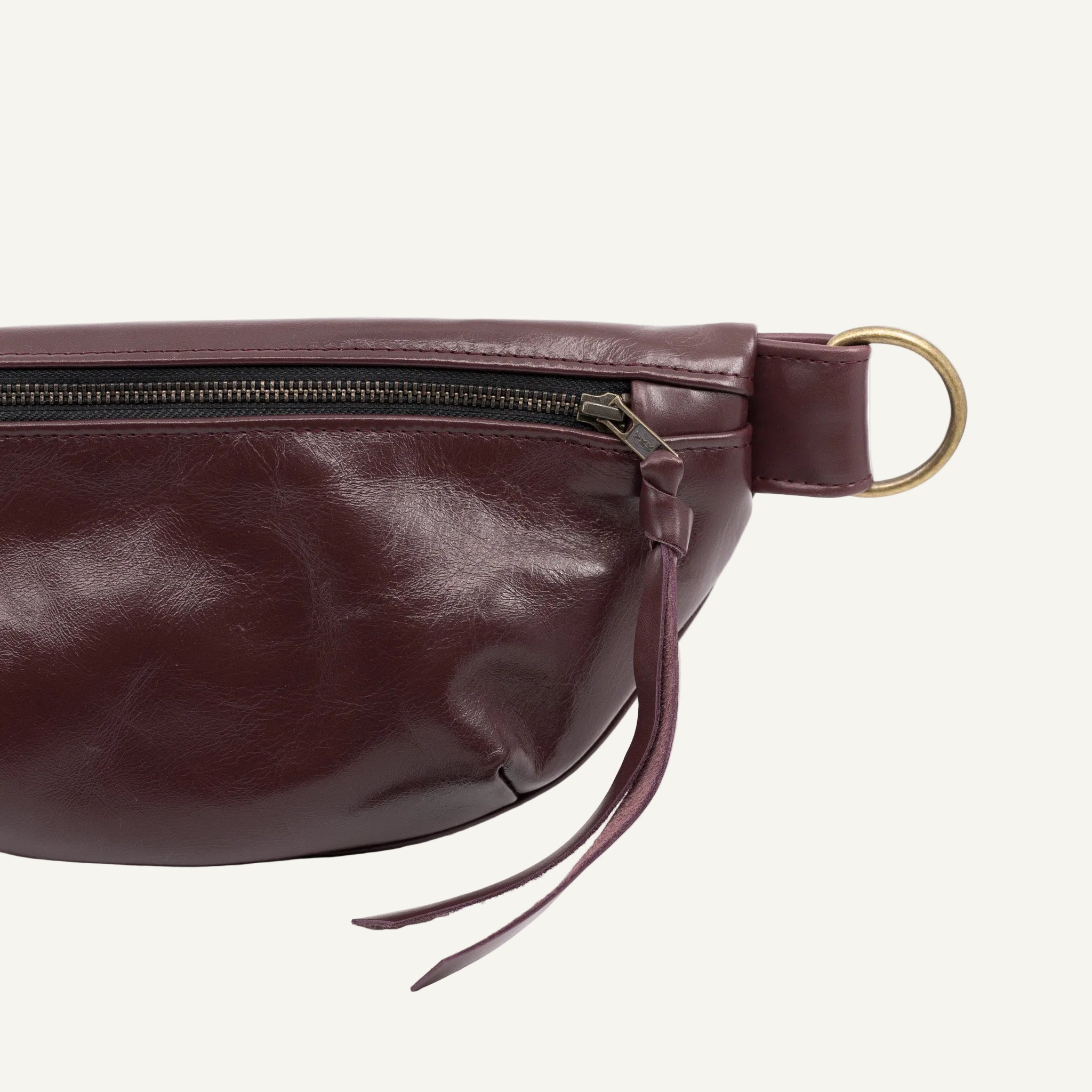 Purple leather waist bag with a gold zipper pull on a white background