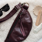 Burgundy leather bag with sunglasses and a comb on a white surface