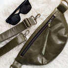 Green leather waist bag with sunglasses on a textured white surface
