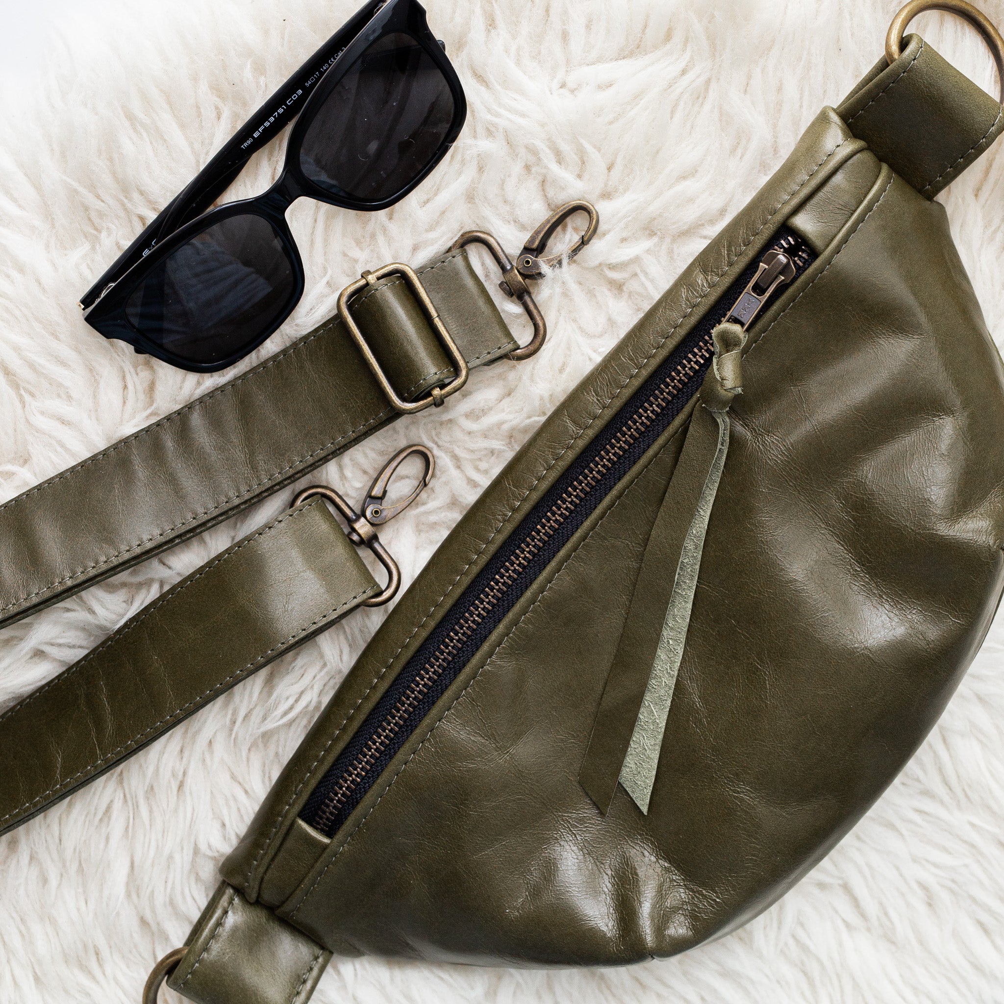 Green leather waist bag with sunglasses on a textured white surface