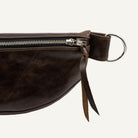 Close-up of a dark brown leather belt bag showing the side zipper, silver metal hardware, on a white background.