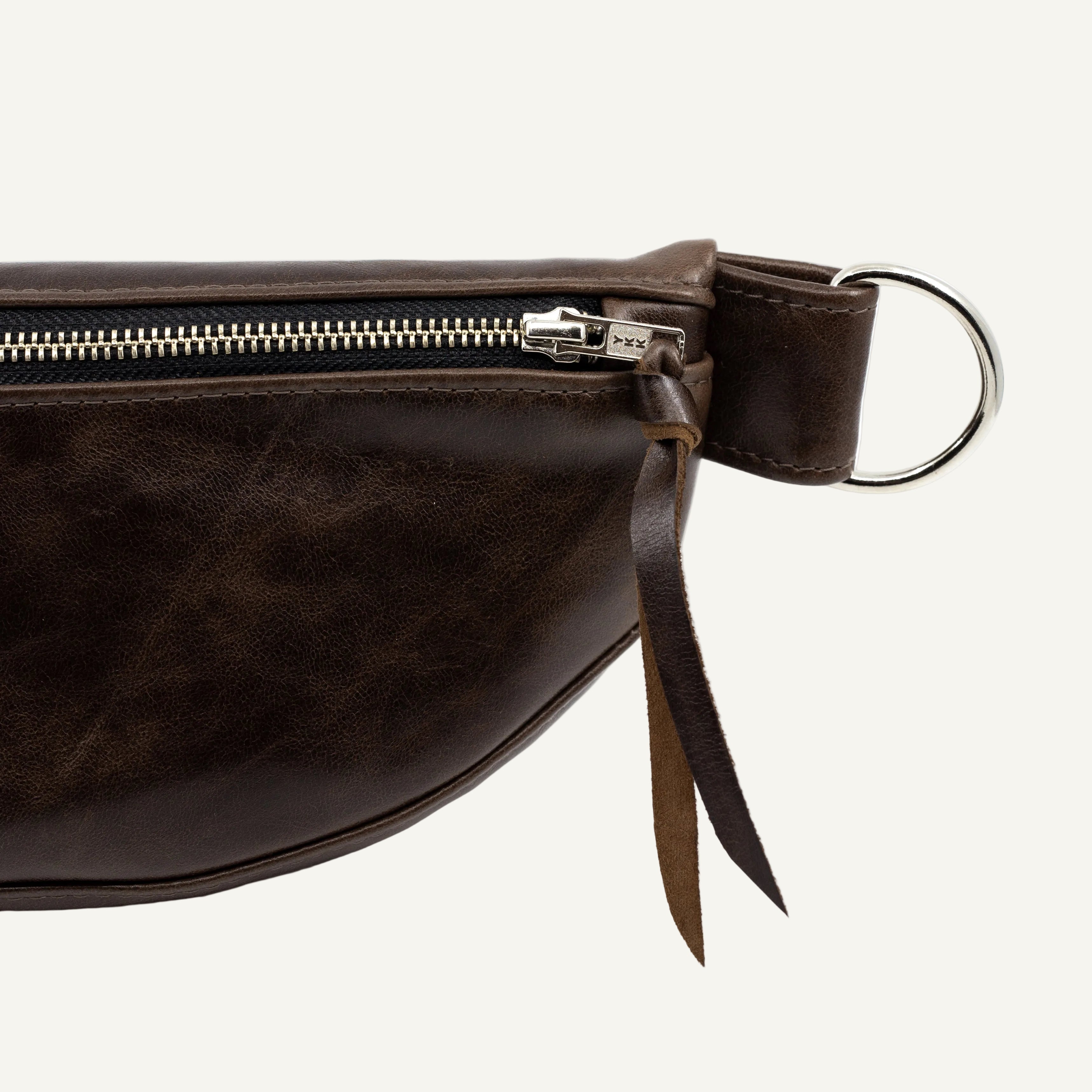 Close-up of a dark brown leather belt bag showing the side zipper, silver metal hardware, on a white background.