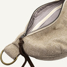 Close-up of a beige woven fabric pouch with an open zipper, showing a gray interior lining, and a brass ring on a white background.