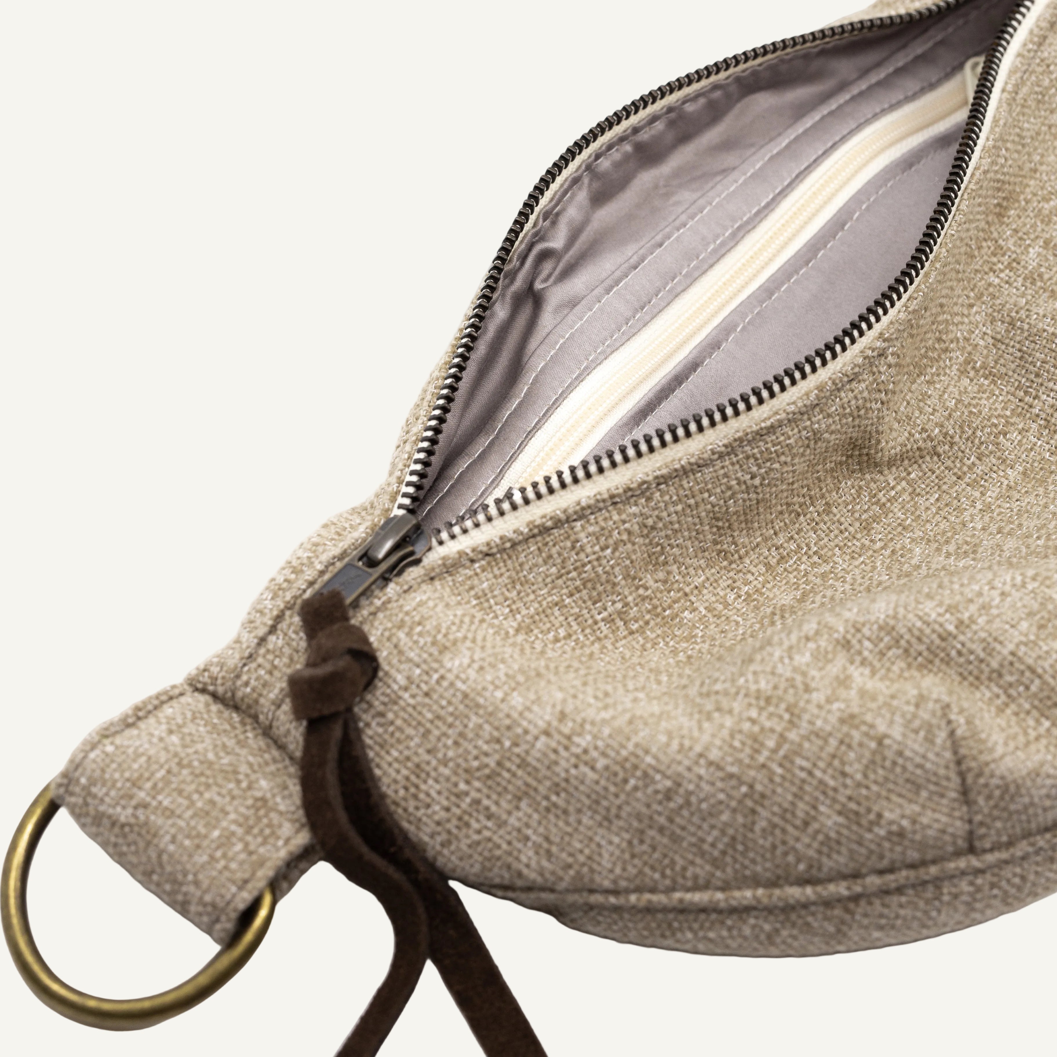 Close-up of a beige woven fabric pouch with an open zipper, showing a gray interior lining, and a brass ring on a white background.