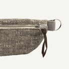 Close-up of a textured gray fabric pouch with a silver zipper, brown leather pull tab, and silver metal ring on a white background.