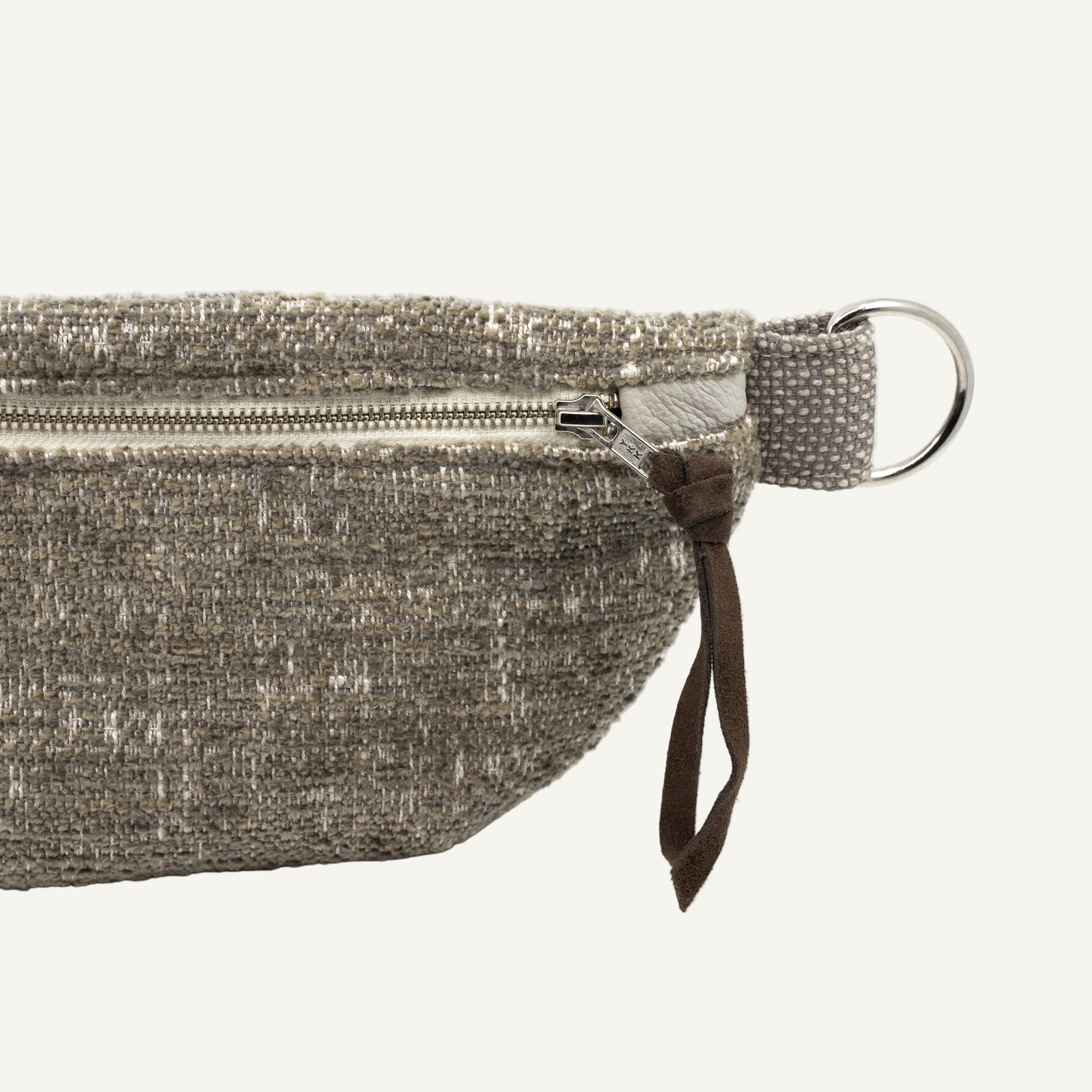 Close-up of a textured gray fabric pouch with a silver zipper, brown leather pull tab, and silver metal ring on a white background.