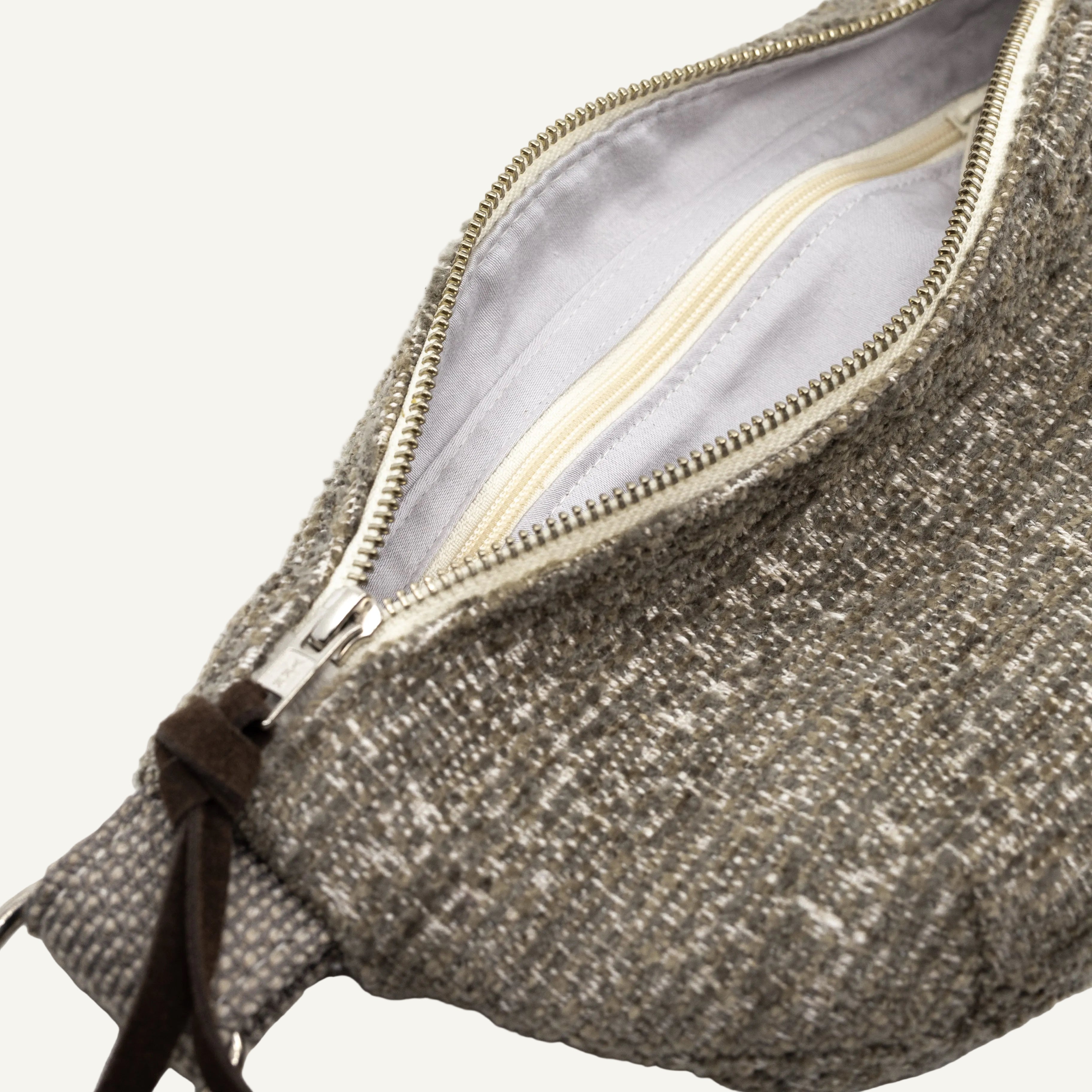 Close-up of a textured gray tweed pouch bag with an open cream zipper, showing the light gray interior lining and a dark brown leather zipper pull detail against a white background.