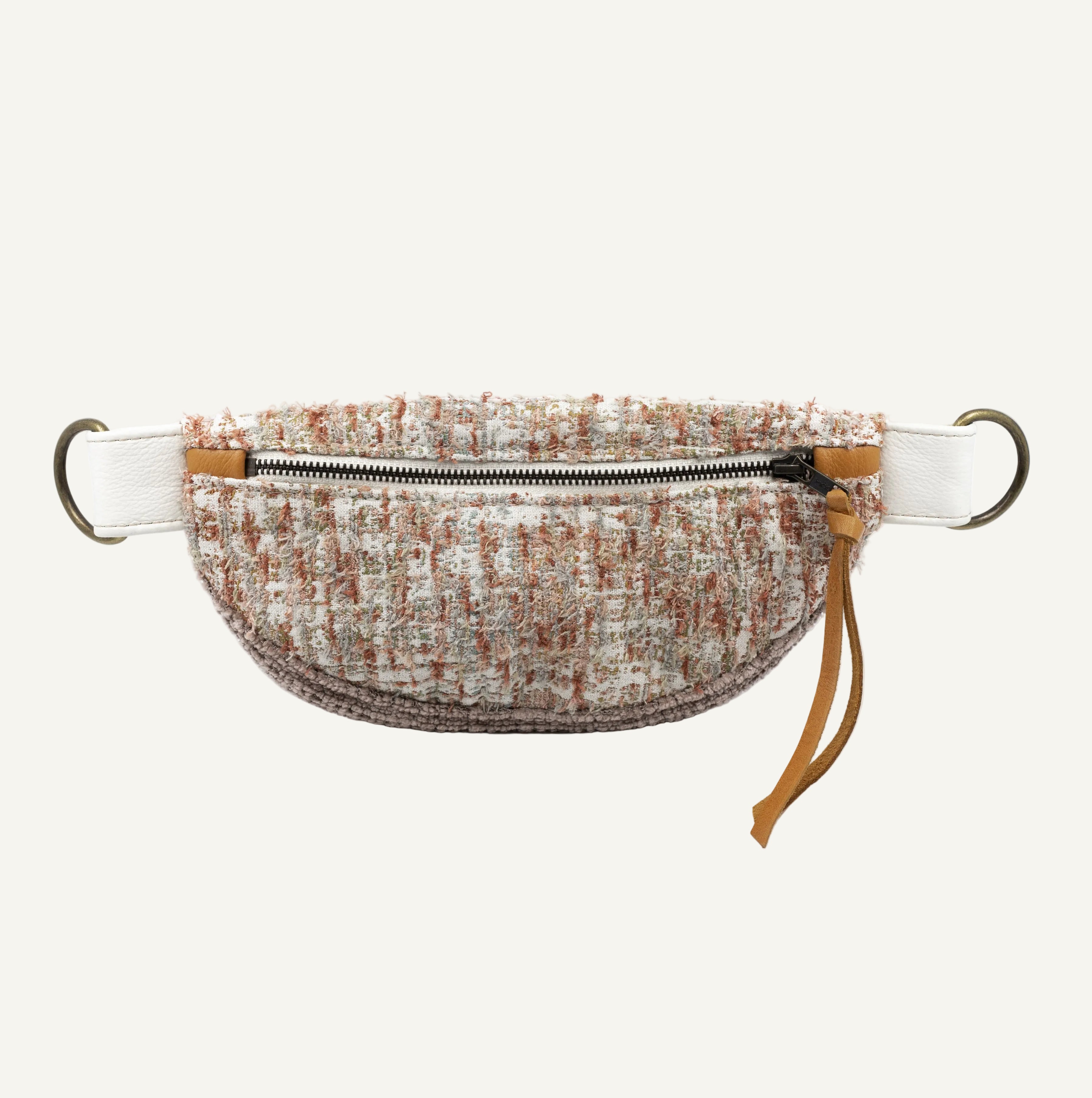 A tweed waist bag with a textured beige, brown, and white bouclé pattern, featuring a white strap with brass hardware and a tan leather zipper pull.