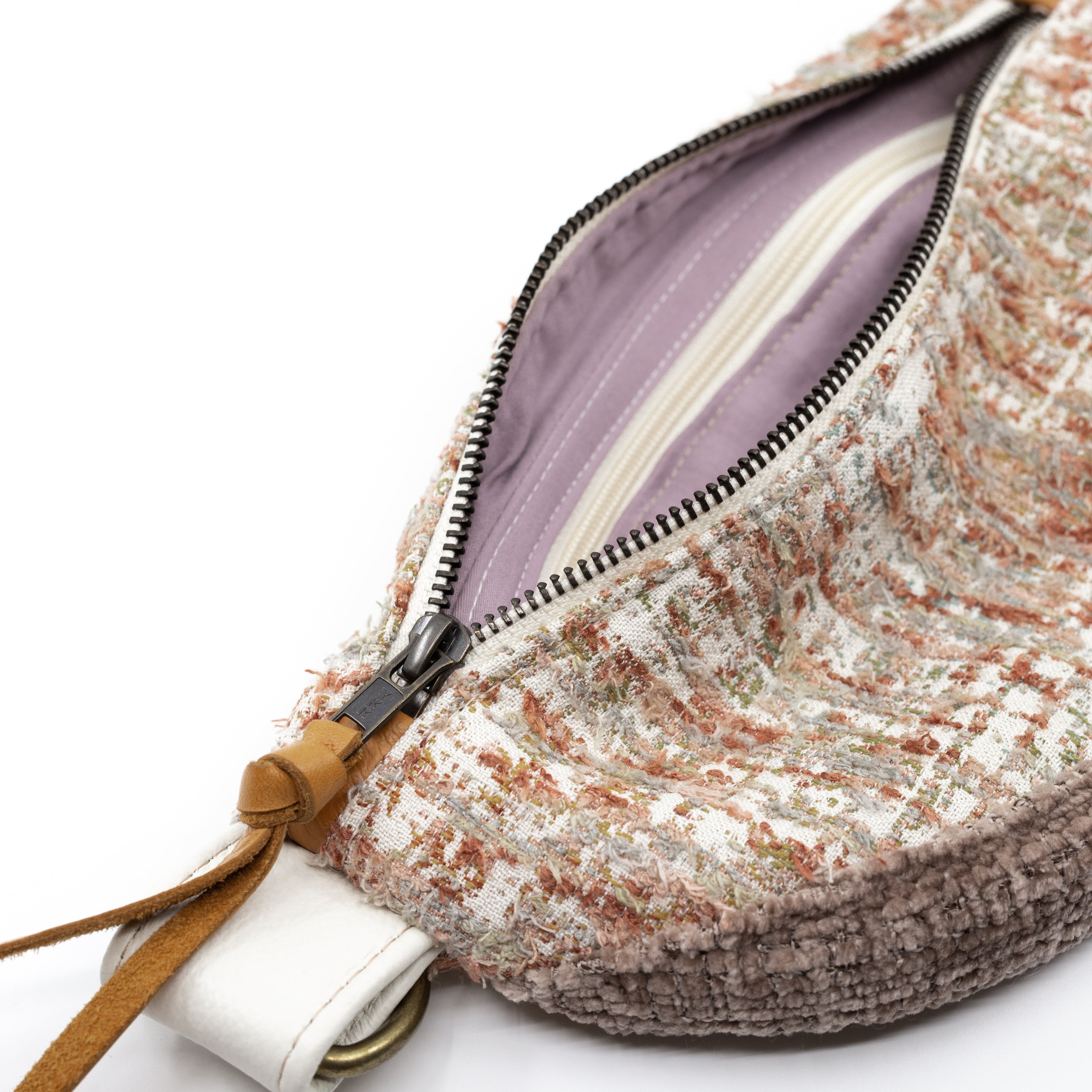 Close-up of a textured tweed pouch bag with a silver zipper, tan leather pull tab, and a light purple interior lining on a white background.
