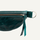 Close-up of a dark teal leather fanny pack with a silver zipper, on a white background.