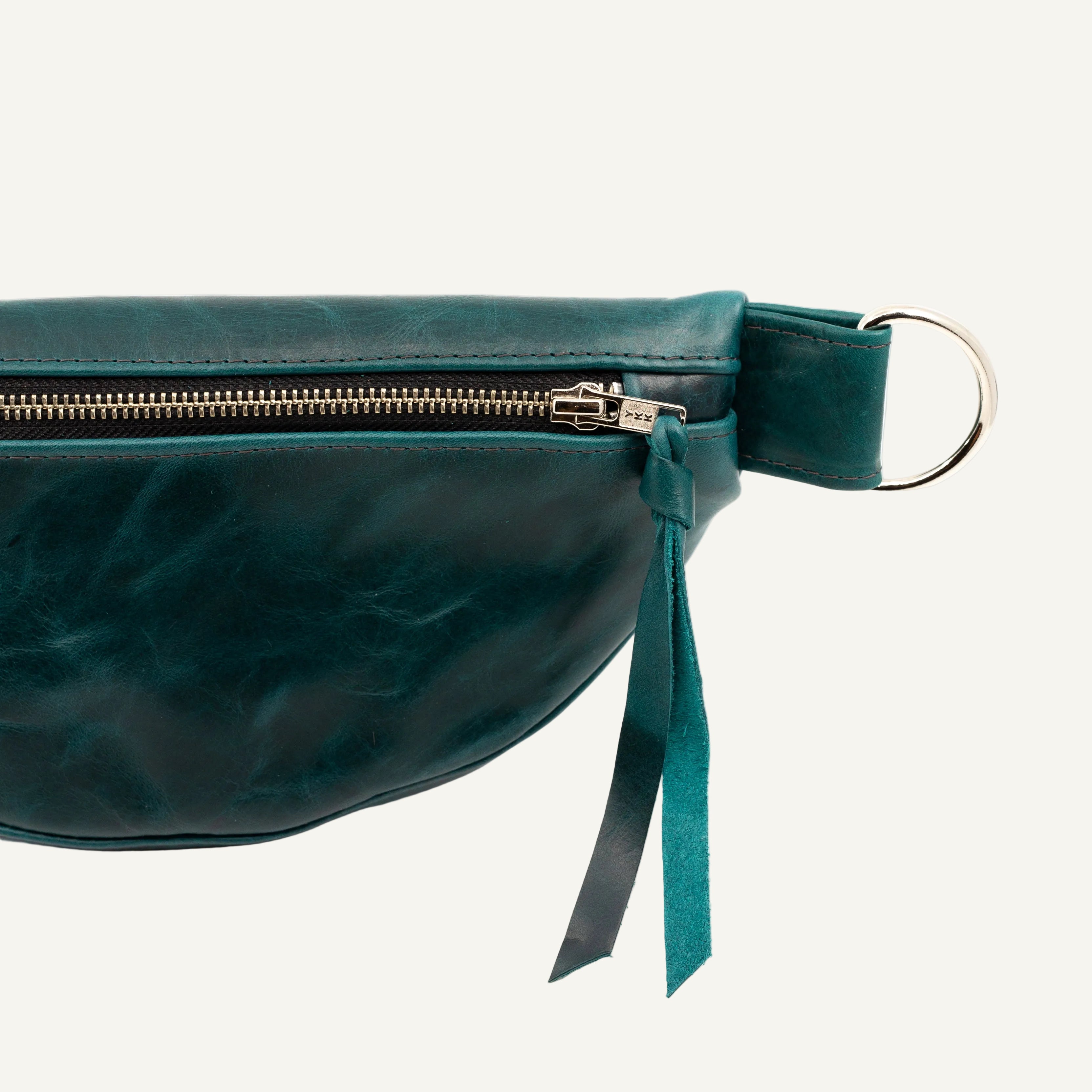 Close-up of a dark teal leather fanny pack with a silver zipper, on a white background.